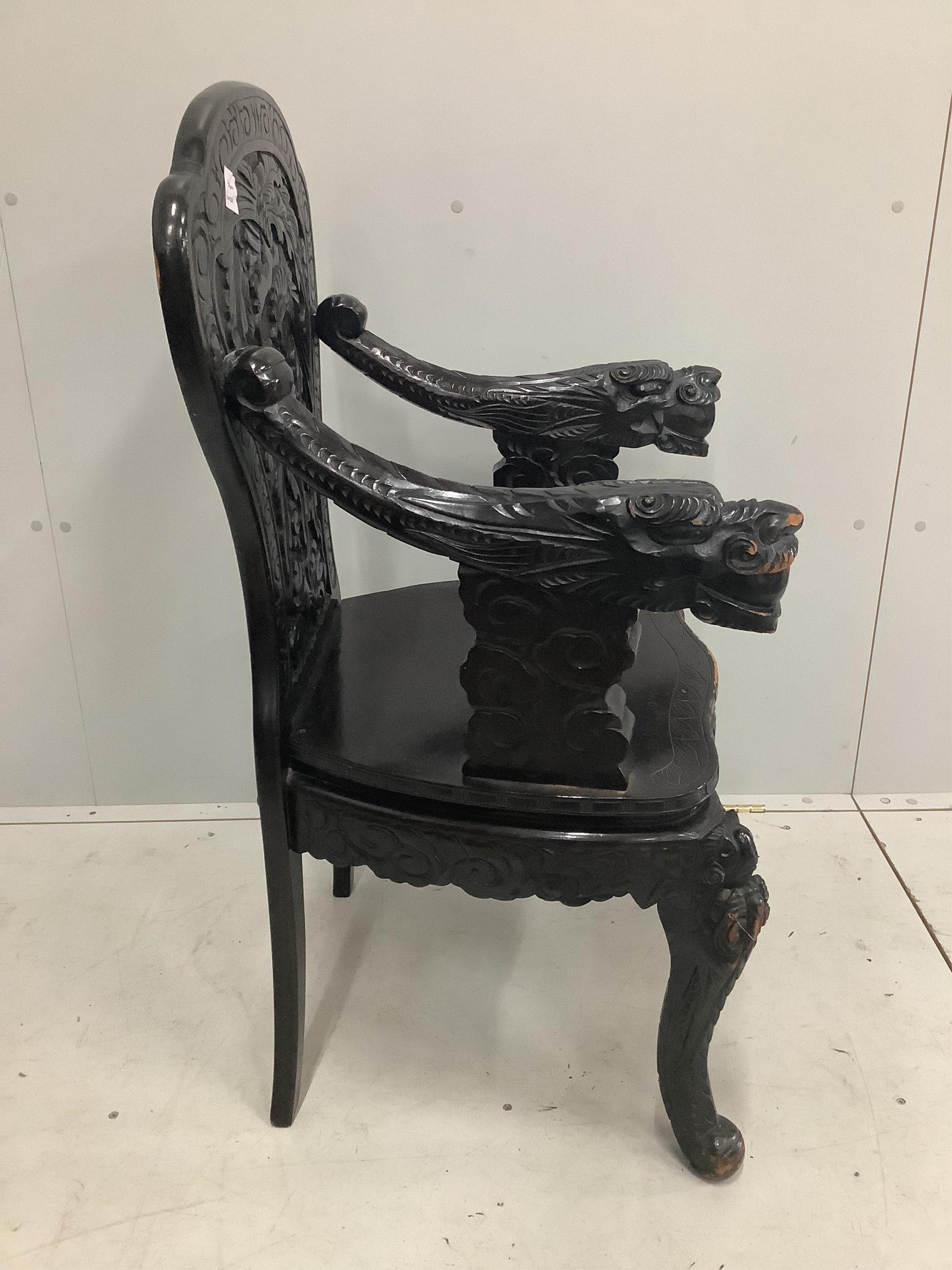An early 20th century Chinese ebonised and carved hardwood elbow chair with dragon arms, width 60cm. Condition - poor